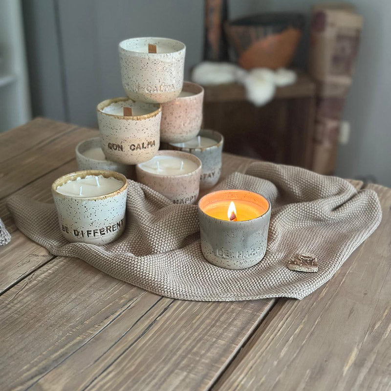 Duftkerze handgemacht im Keramikbecher in einem warmen Wohnzimmer-Setting mit bunten Kerzen.