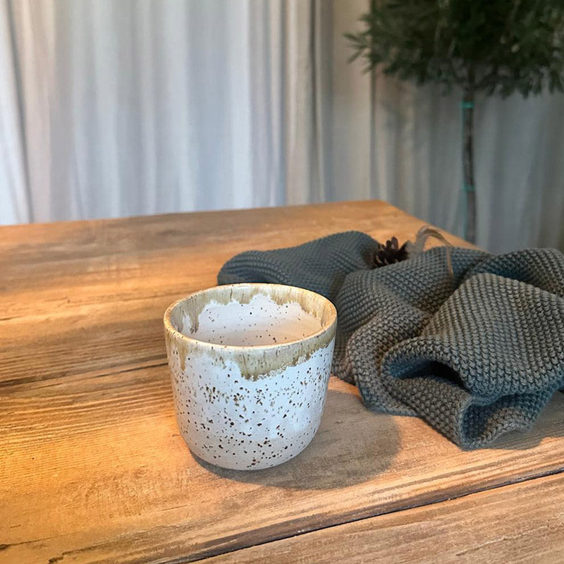 Duftkerze handgemacht im Keramikbecher auf einem Tisch mit einem Handtuch und einer grünen Dekoration.