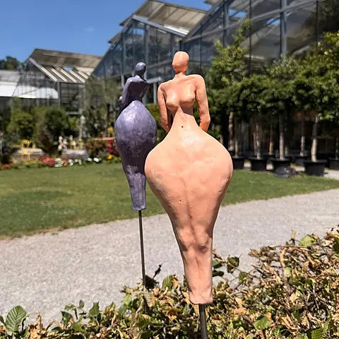 Keramikfiguren in gelborange im Vordergrund und in Fliederfarben im Hintergrund, abstrakte weibliche Silhouetten auf Steinterrasse