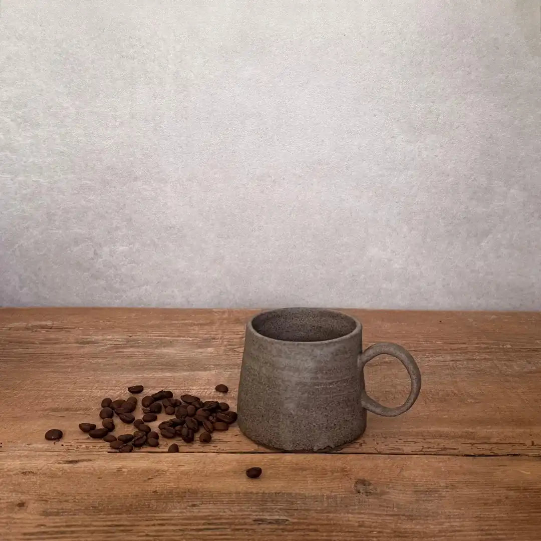 AREIA Cappuccino-Tasse in Salt & Pepper neben Kaffeebohnen auf Holztisch