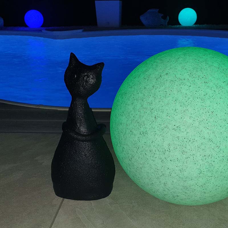 Keramikkatze in dunkelblau neben grünem ball vor Swimmingpool