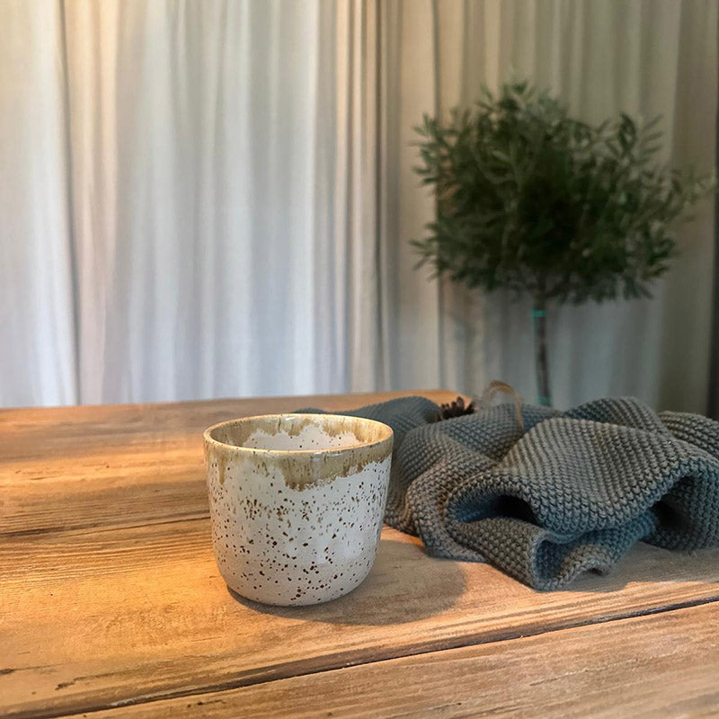 Duftkerze handgemacht im Keramikbecher Sojawachs im stimmigen Ambiente auf einem Holztisch.